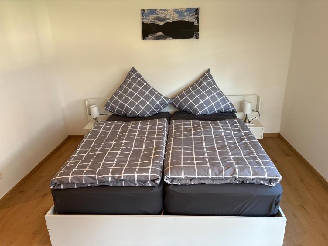 Doppelbett mit grauem Bettzeug und zwei Nachttischen mit Lampen.