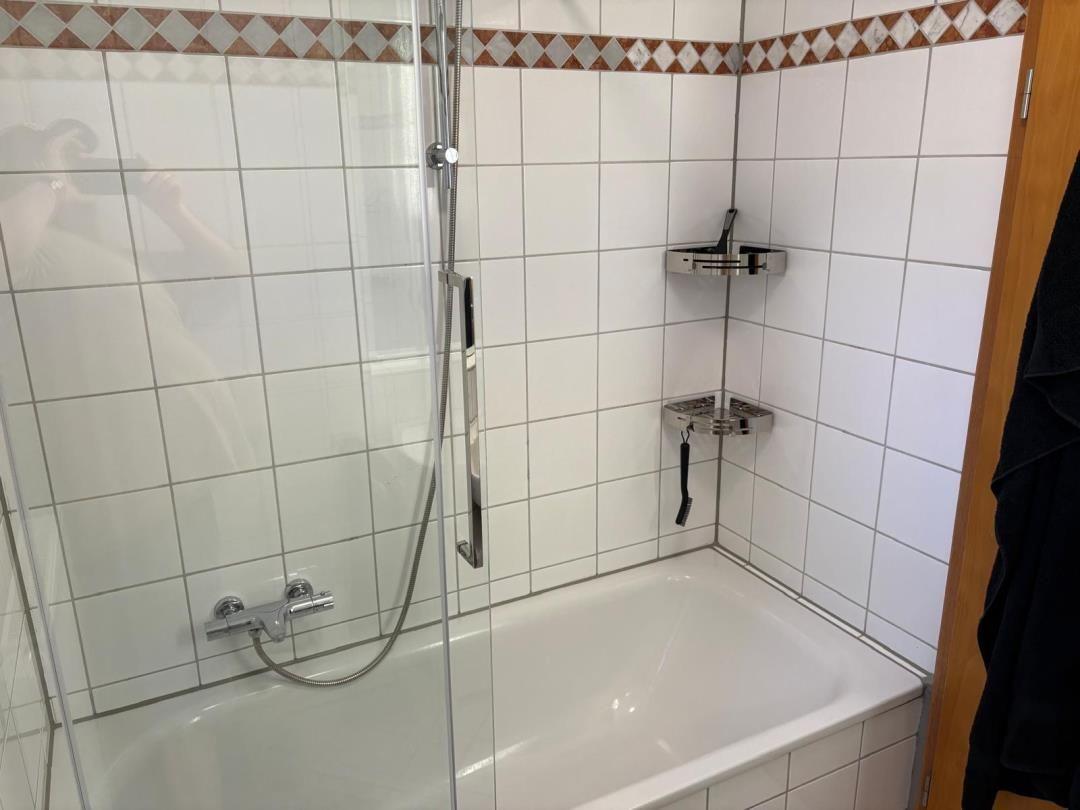 Bad mit Dusche und Badewanne, weiße Fliesen und Chromhalterungen.