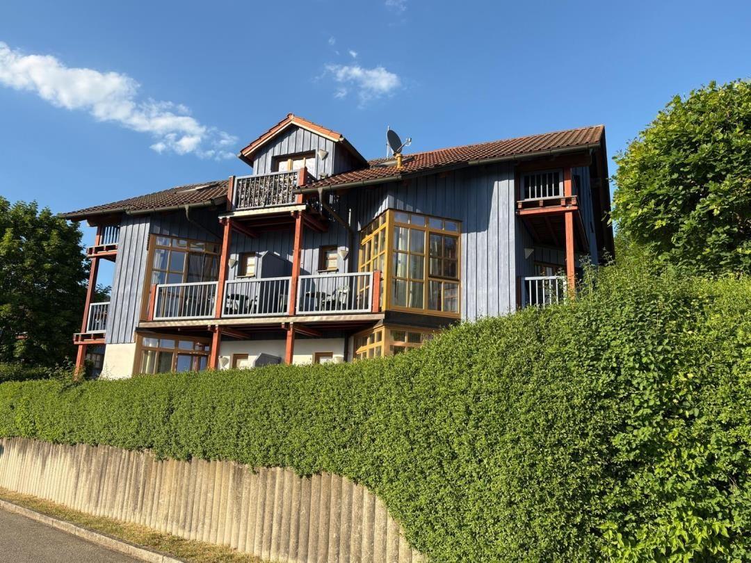 Ein zweistöckiges Haus mit Balkonen und Dachterrasse, umgeben von grüner Hecke.