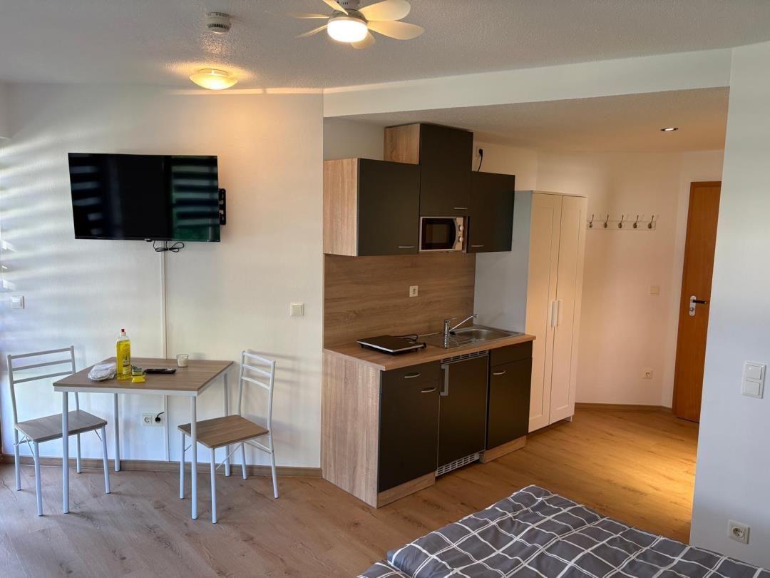 Küche mit Arbeitsplatte, Spüle und Mikrowelle. Esstisch mit zwei Stühlen. TV an der Wand.