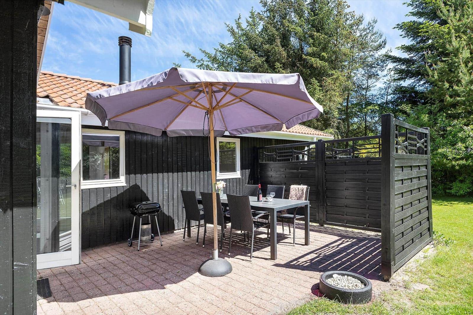 Terrasse mit Tisch, Stühlen und Sonnenschirm. Grill und Pflanzen sind vorhanden.