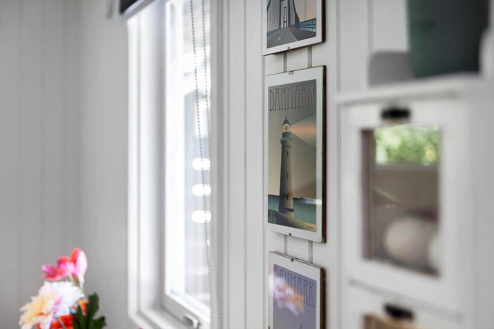 Wand mit drei Bildern von Dänemark, einem Fenster und Blumen im Vordergrund.