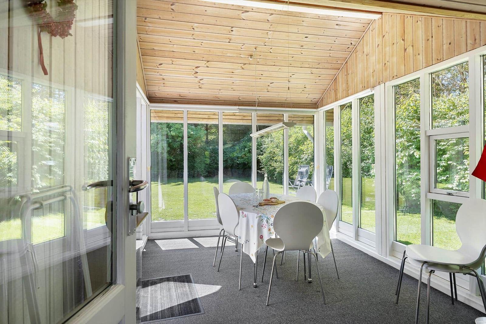 Essbereich mit Tisch und Stühlen, umgeben von großen Fenstern mit Blick auf Garten.