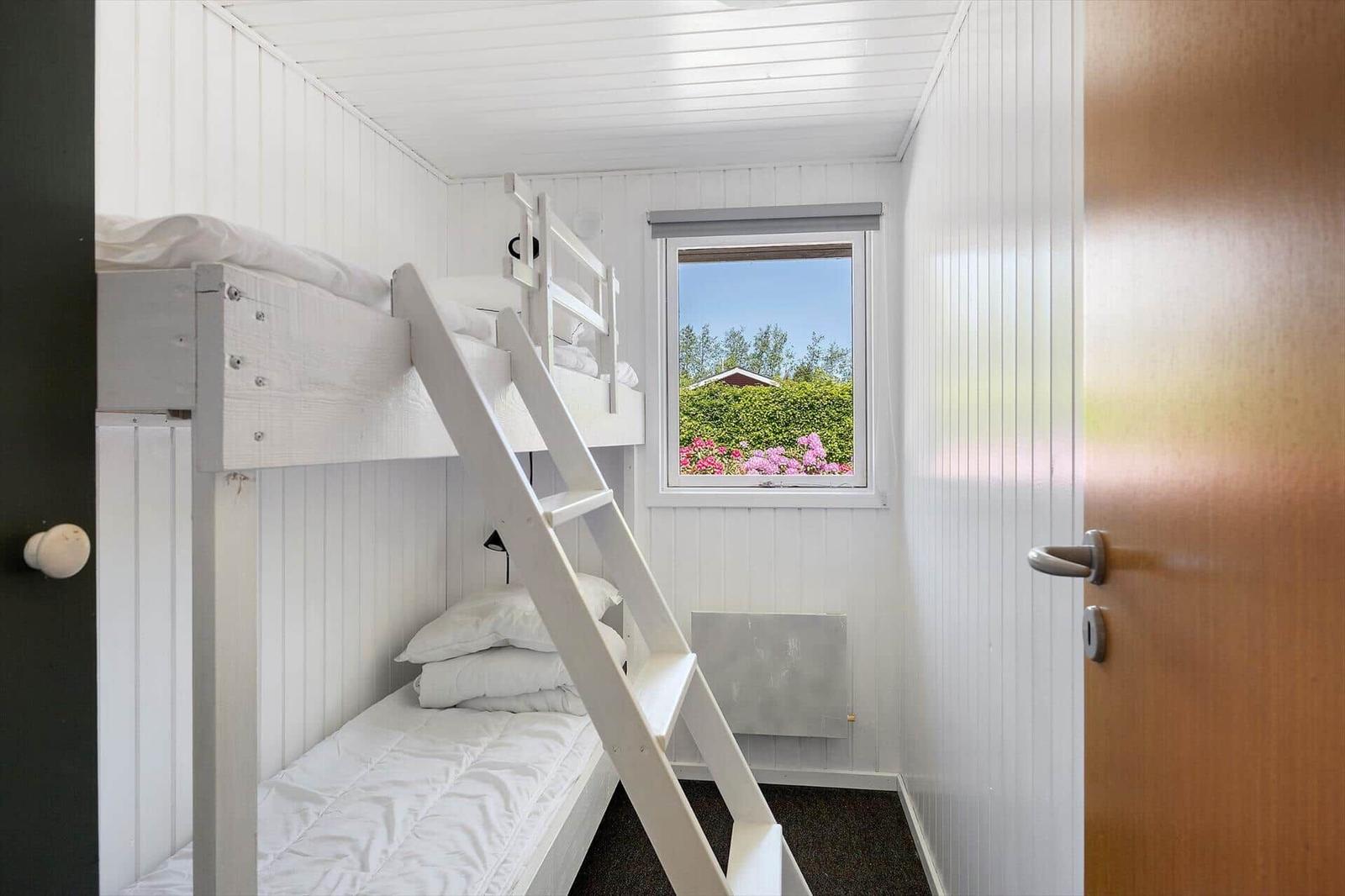 Zimmer mit Doppelstockbett, Fenster mit Blick auf Grün und Blumen.