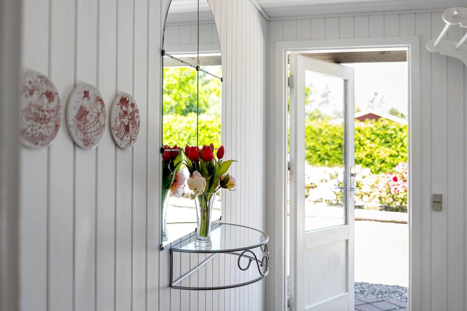 Eingangsbereich mit Spiegel, Blumen und dekorativen Platten an weißer Wand.