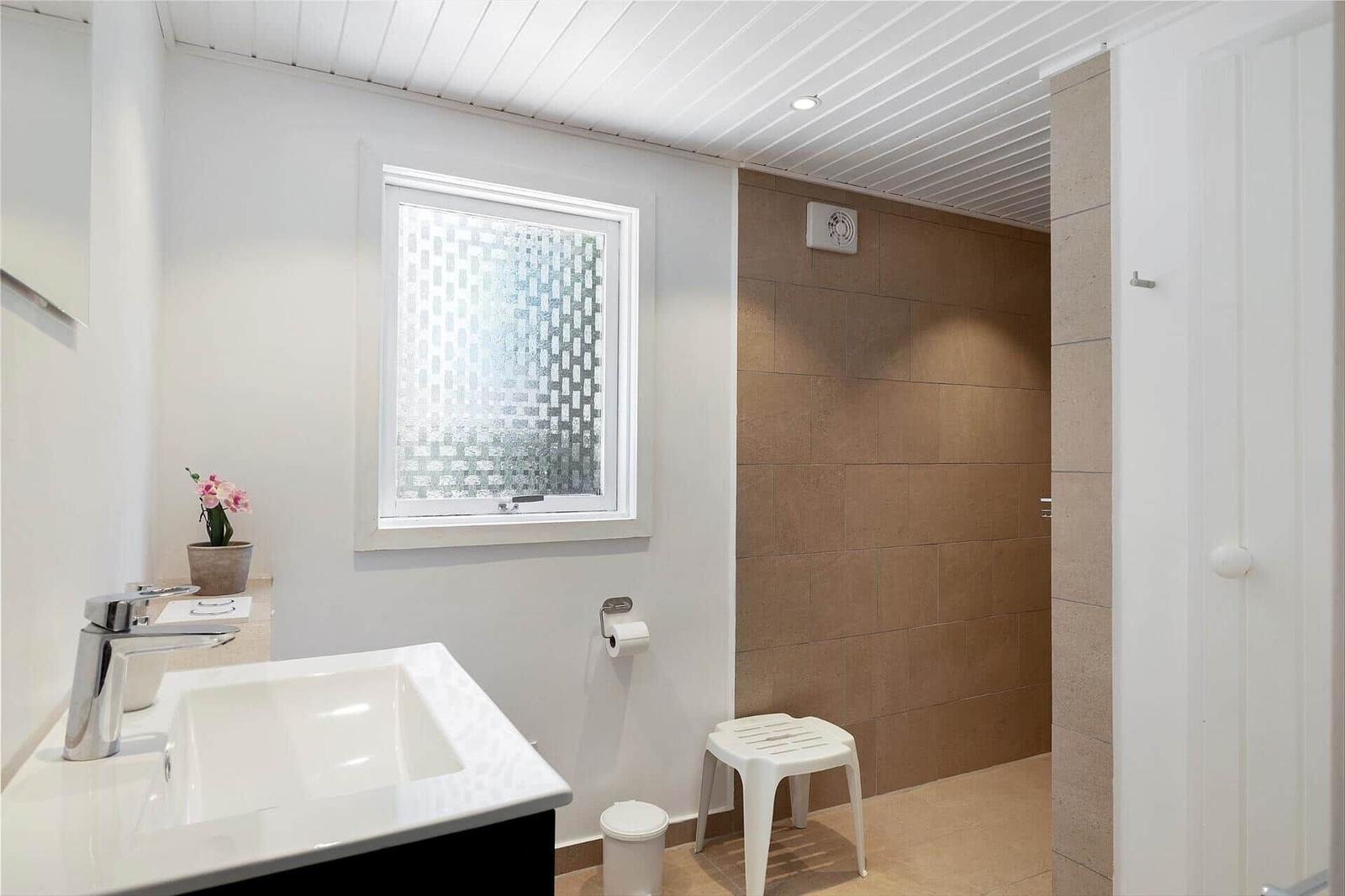 Bad mit Waschbecken, Fenster und Dusche mit braunen Fliesen.