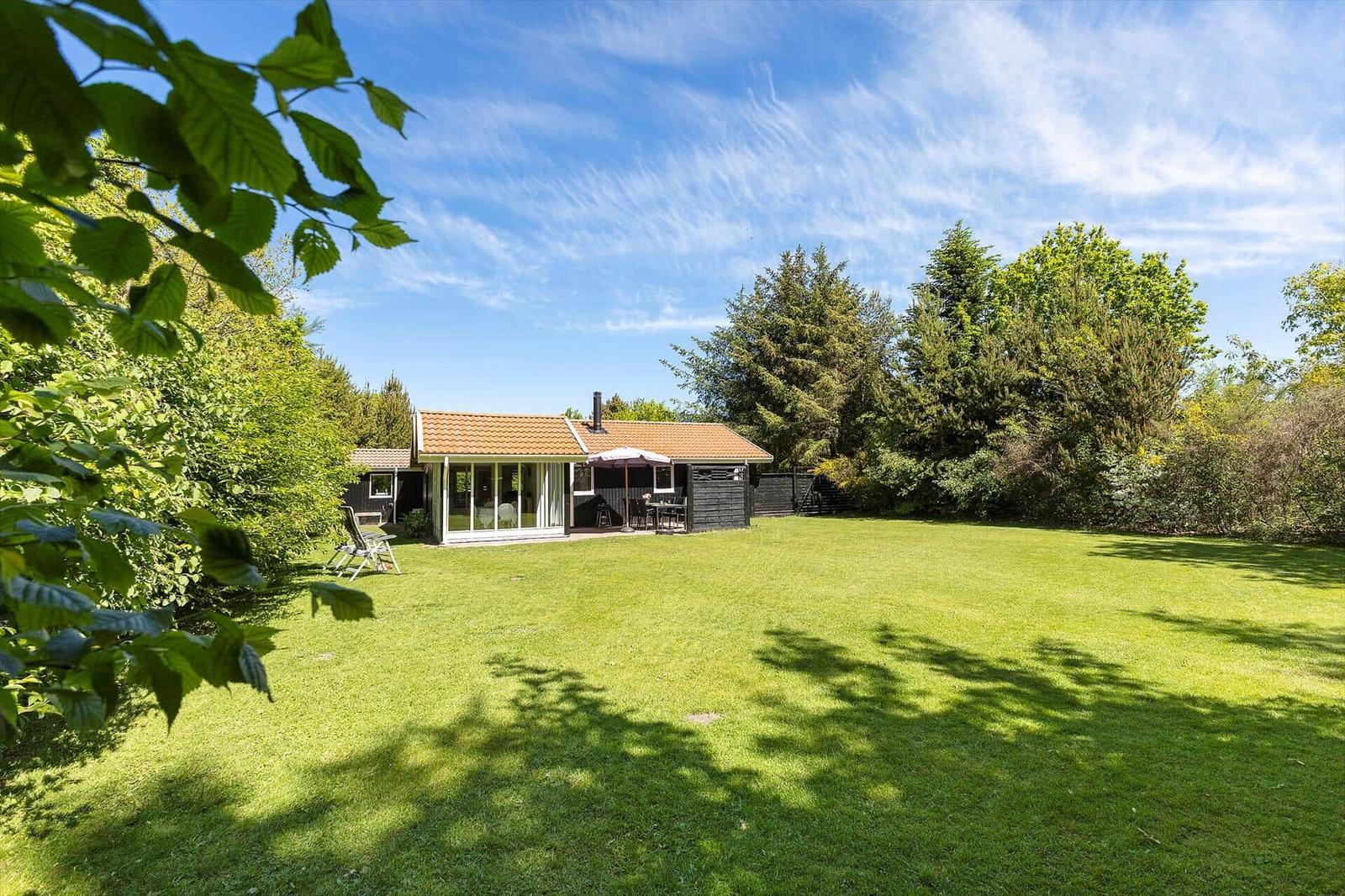 Haus mit Garten, Terrasse und Grillplatz unter Bäumen.
