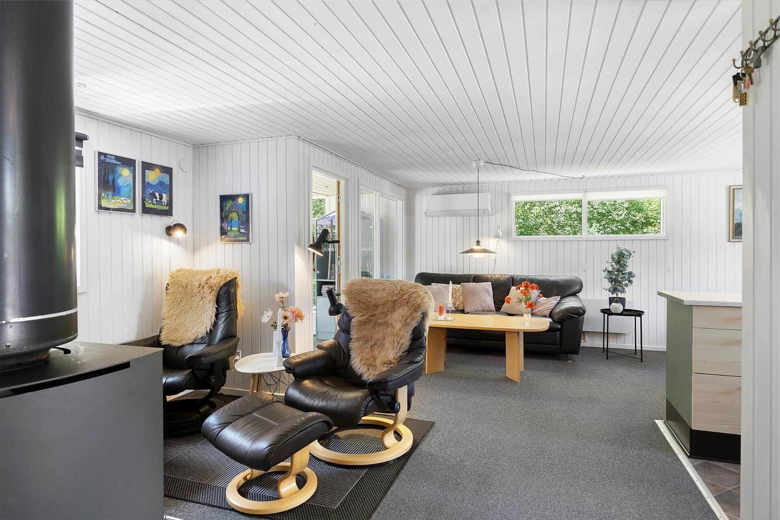 Wohnraum mit zwei schwarzen Sesseln, Sofa und Holztisch. Weiße Wände und Decke.