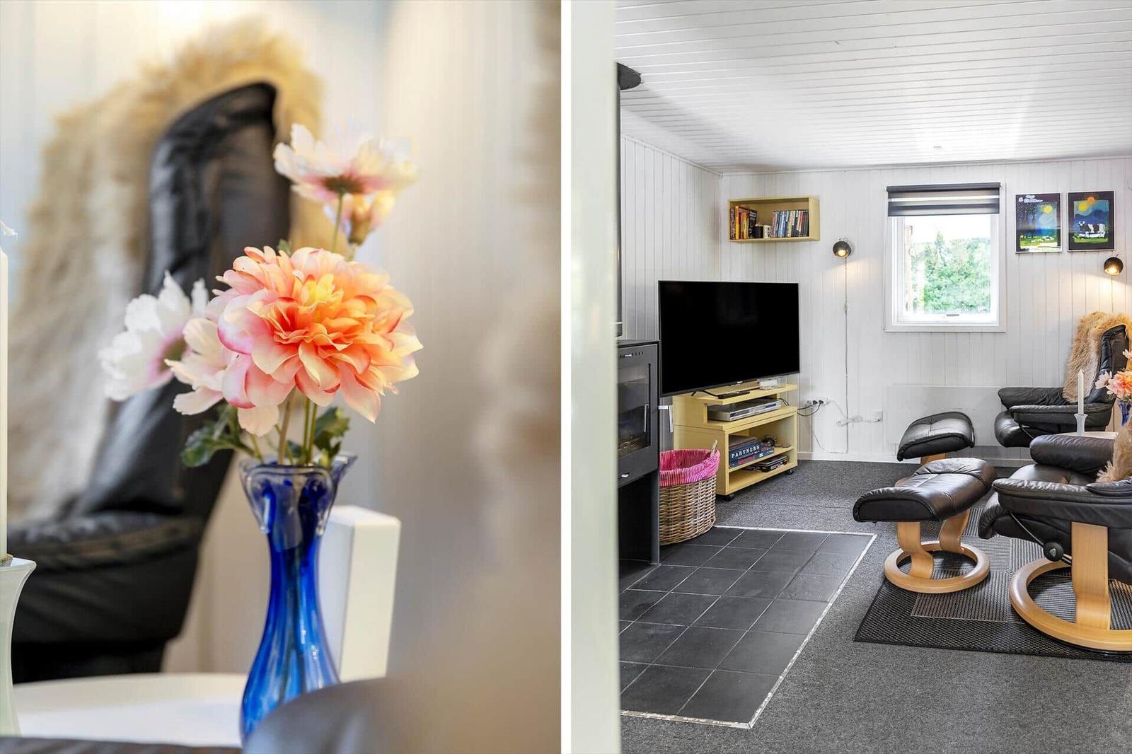 Wohnzimmer mit Fernseher, Sitzgelegenheiten und Fenster. Blumen in Vase im Vordergrund.