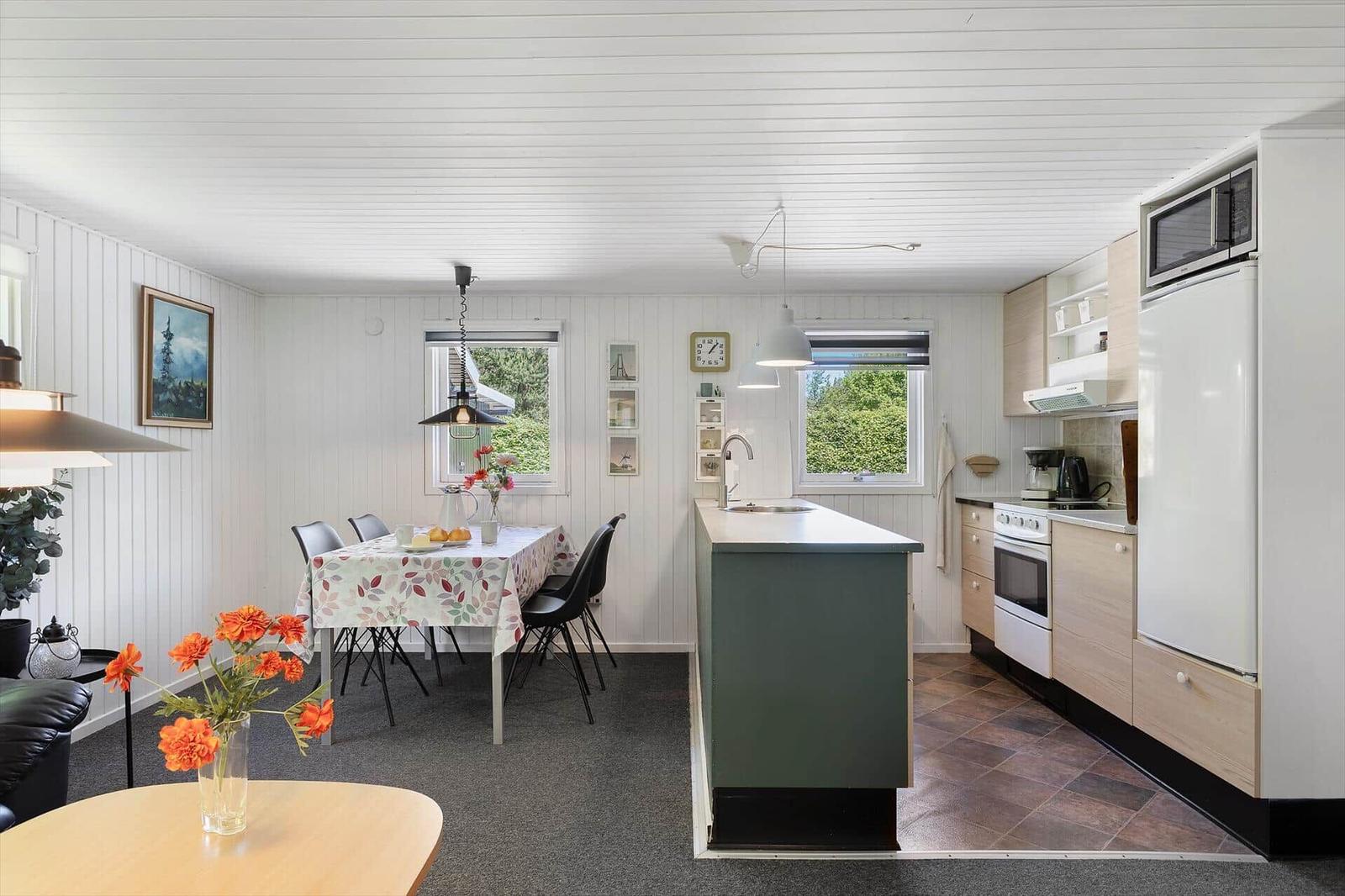 Küche mit Essbereich, Kücheninsel und Fenstern. Weiße Wände, Holzschrank und Kühlschrank.