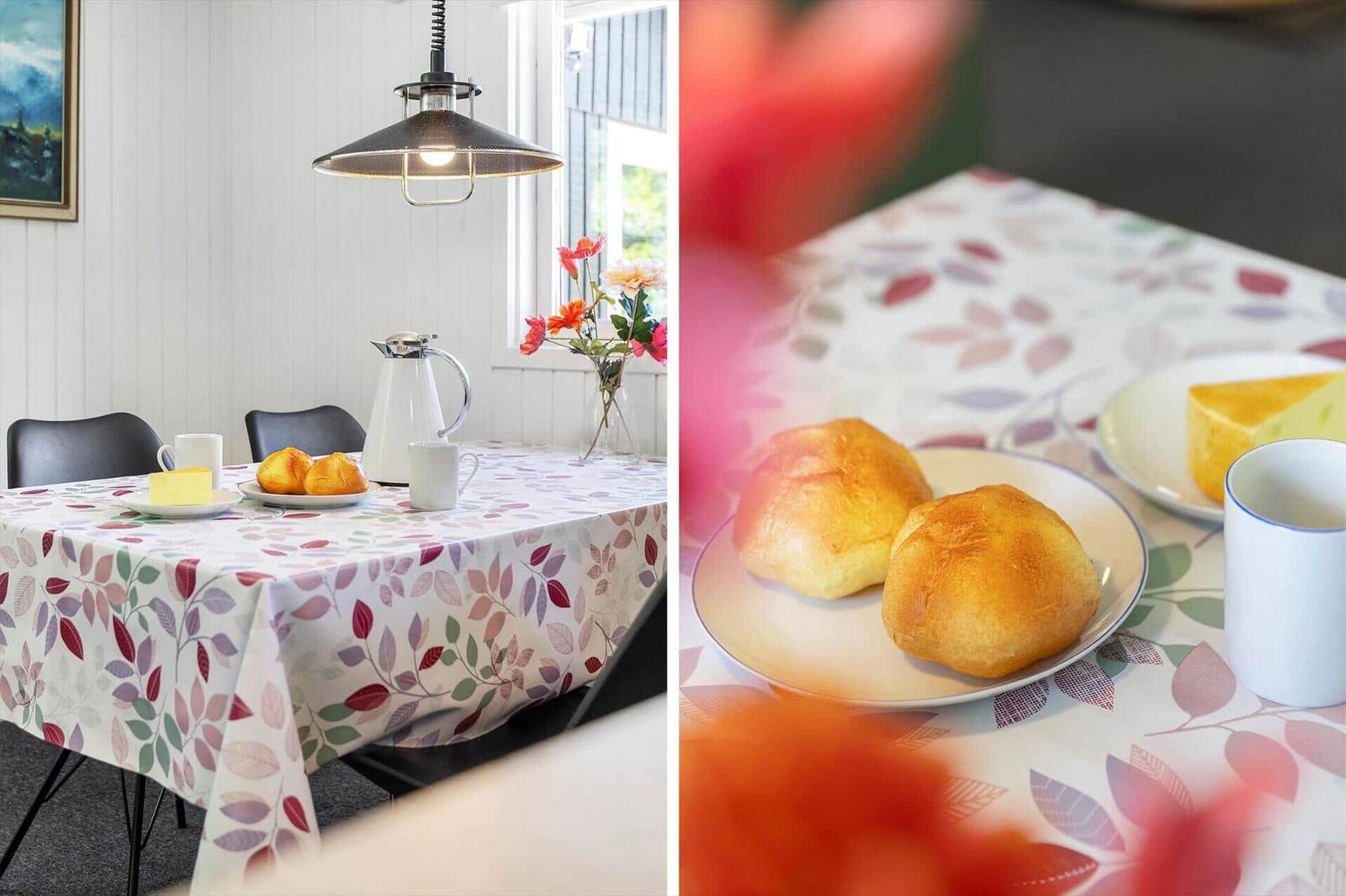 Tisch mit Blättermuster, Brötchen, Kaffee und Käse. Hängelampe und Blumen im Hintergrund.