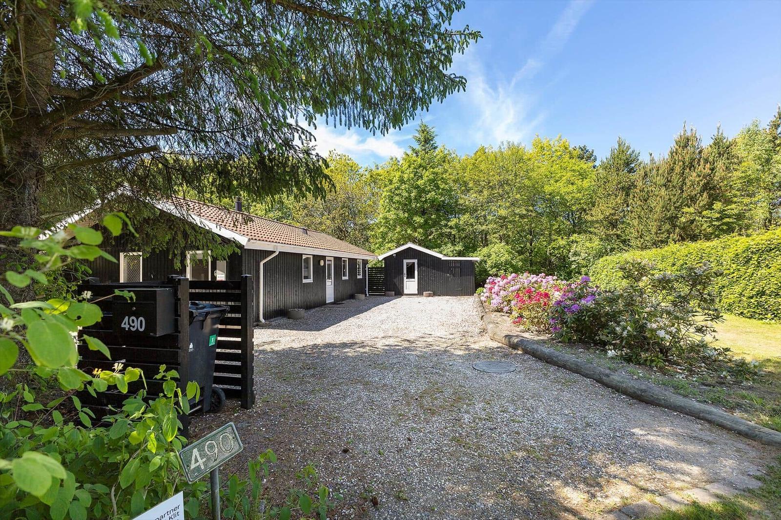 Haus mit grauem Kiesweg, blühenden Sträuchern und grüner Umgebung.