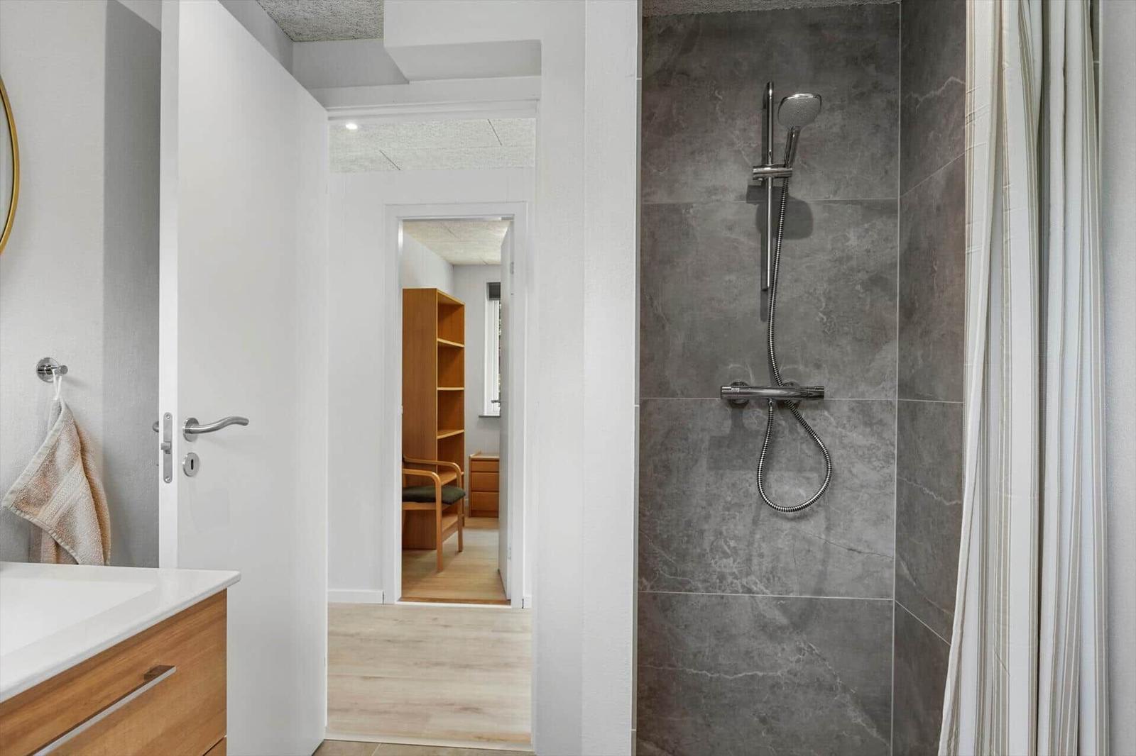 Badezimmer mit Dusche und Waschbecken. Durchgang zur Schlafzimmer mit Holzmöbeln.