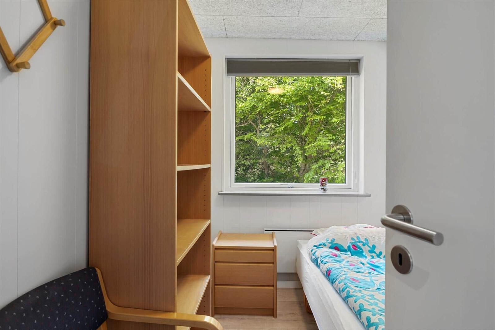 Schlafzimmer mit Bett, Schrank und Fenster mit Blick auf Bäume.