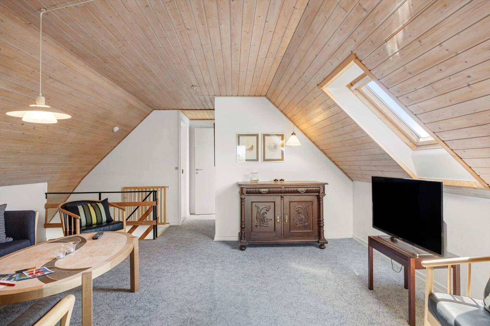 Dachgeschosswohnung mit Holzdecke, TV, Schrank und Sitzgelegenheiten.