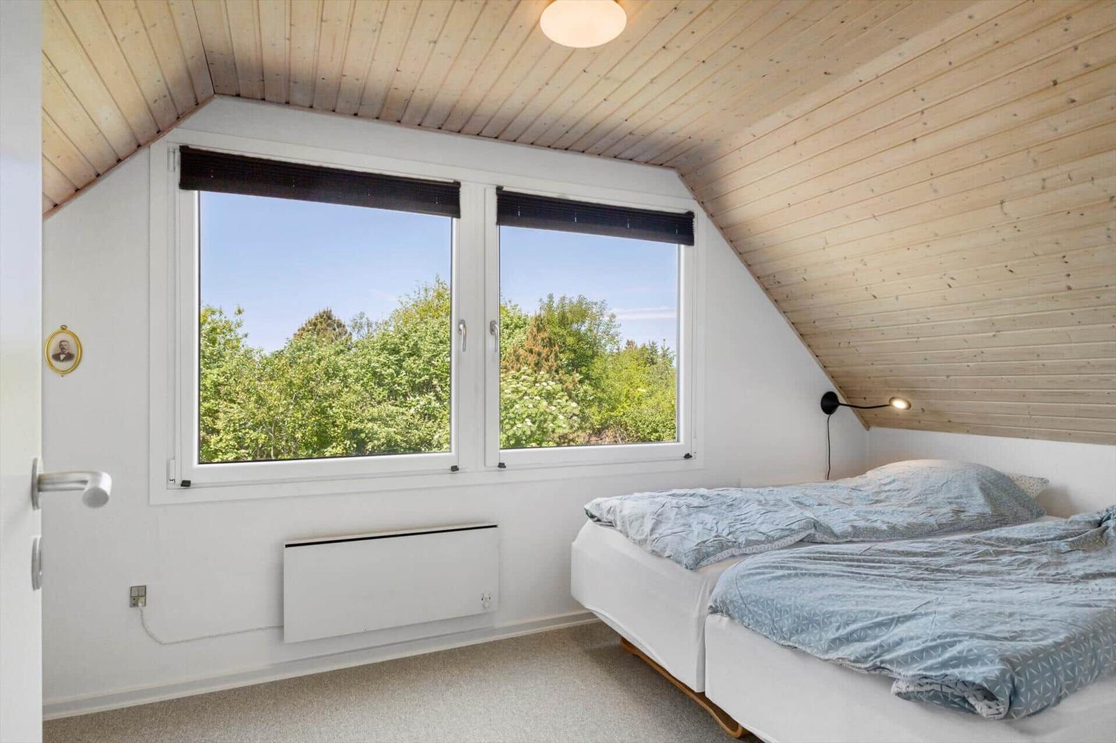 Schlafzimmer mit Dachschrägen, großem Fenster und Bett mit blauer Bettwäsche.