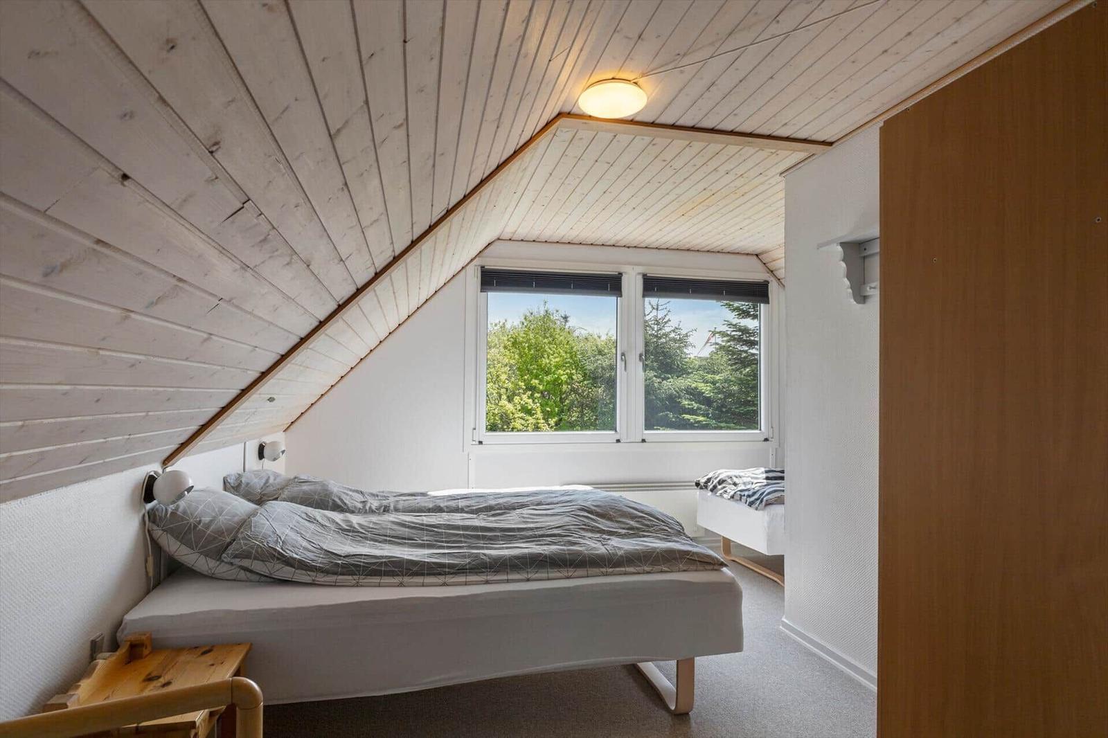 Schlafzimmer mit Dachschrägen, Bett, Fenster und Kleiderschrank.
