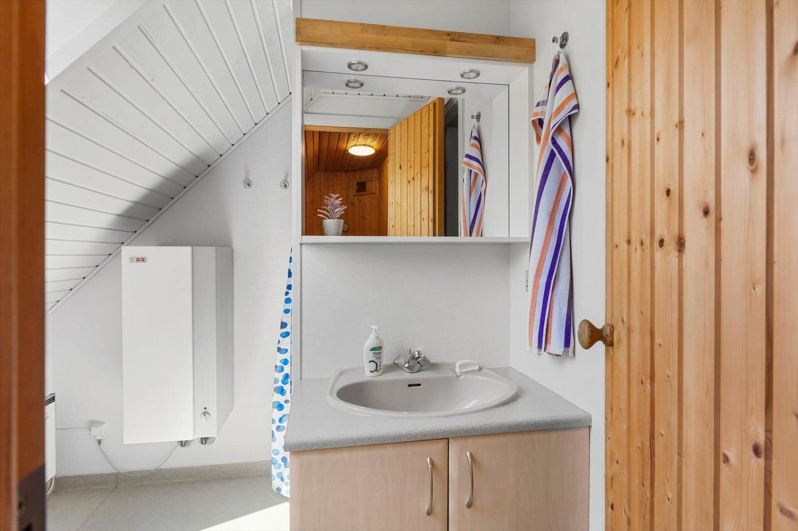 Badezimmer mit Waschbecken, Spiegel und Duschabtrennung. Holzwände und Dachschrägen sichtbar.