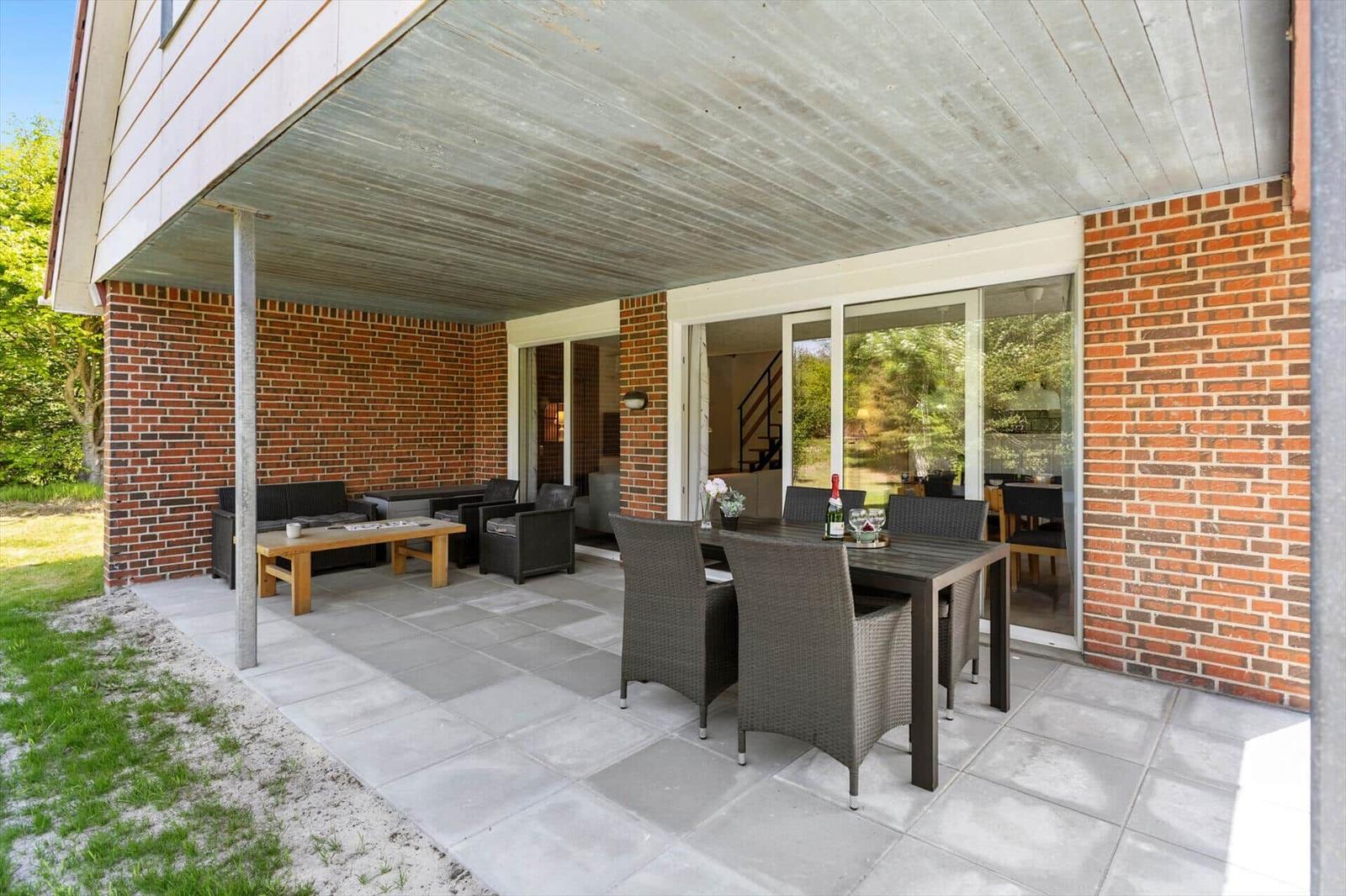 Terrasse mit Sitzgruppe und Esstisch unter Dach. Blick in das Haus über Glastüren.