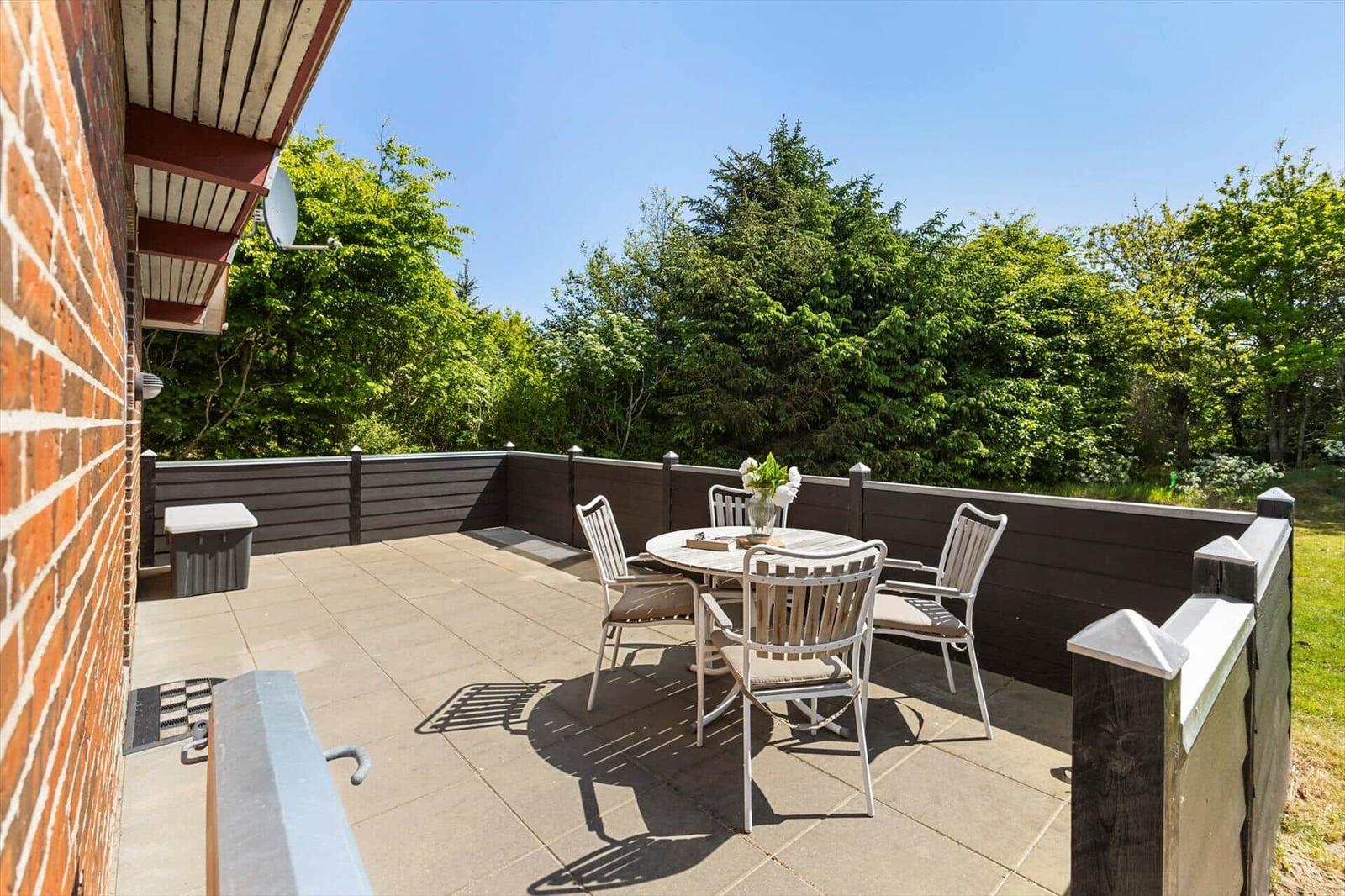 Terrasse mit Tisch und Stühlen, umgeben von grüner Vegetation und Holzgeländer.