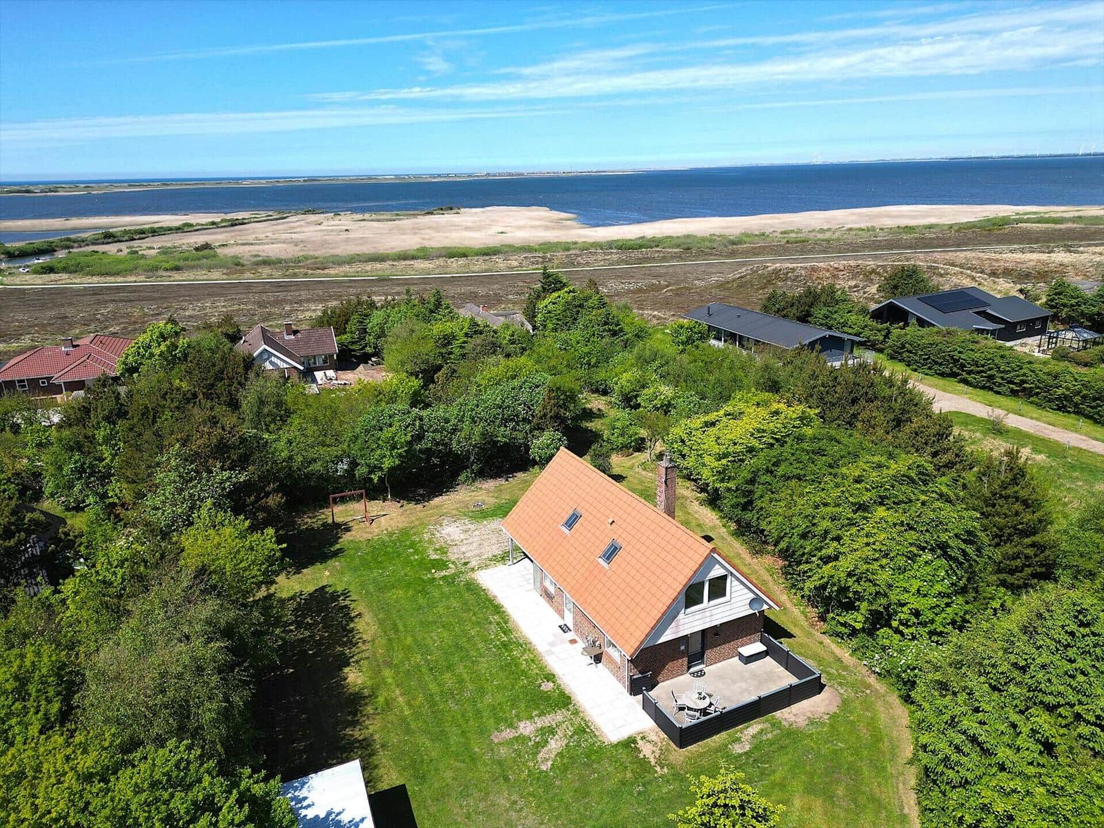 Haus mit Terrasse, umgeben von Grün, Blick auf Meer und Strand.