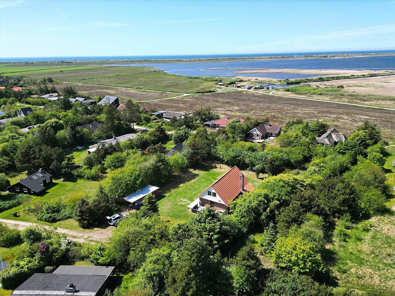 Haus mit rotem Dach, umgeben von Grünflächen und Bäumen. Im Hintergrund See und Horizont.