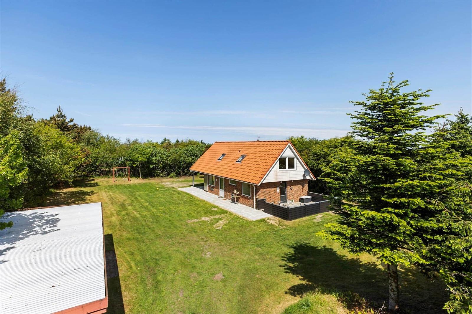 Ein Haus mit rotem Dach und Garten umgeben von Bäumen.