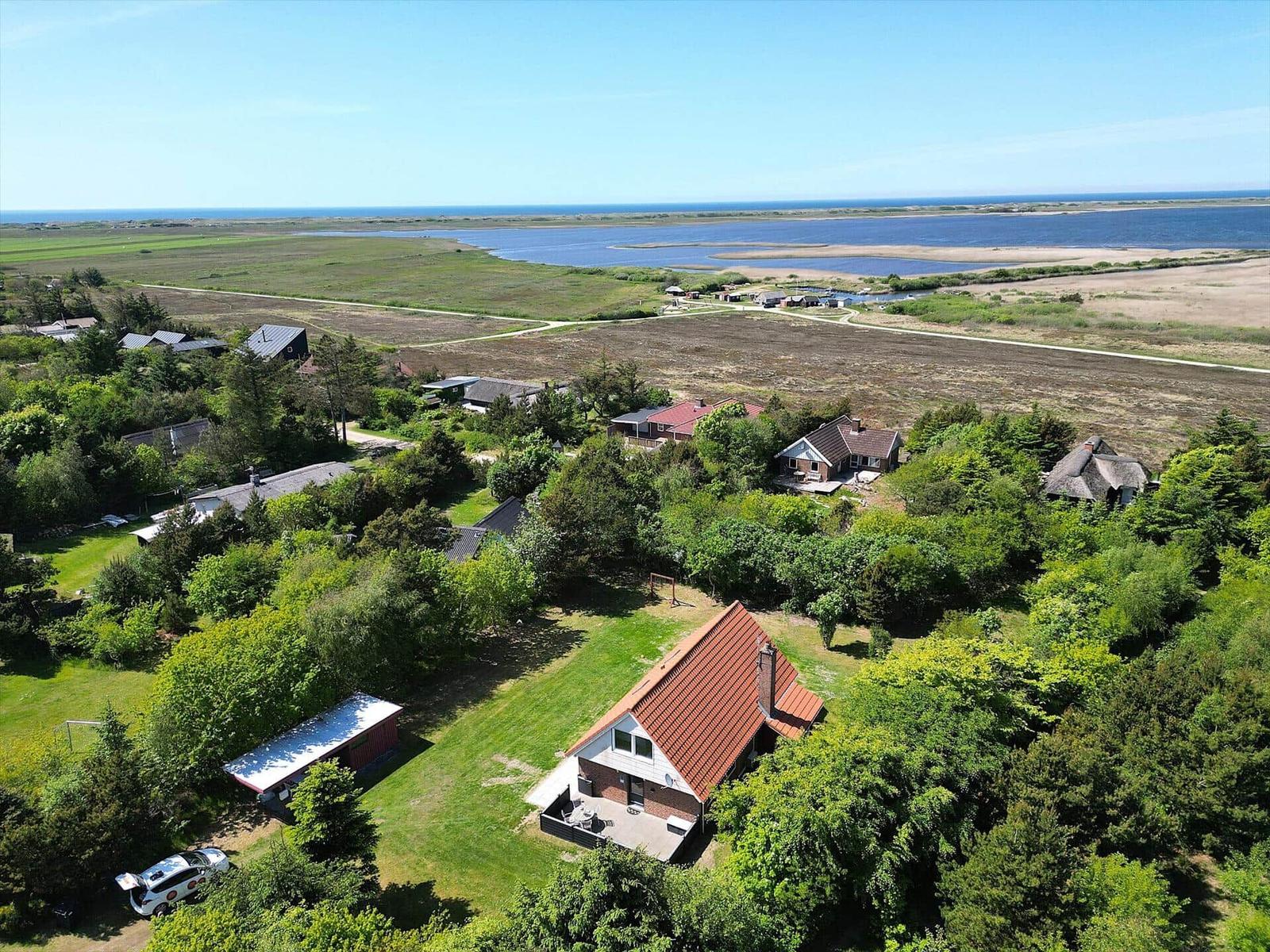 Haus mit rotem Dach in grüner Umgebung, Blick auf Wasser und Strand.
