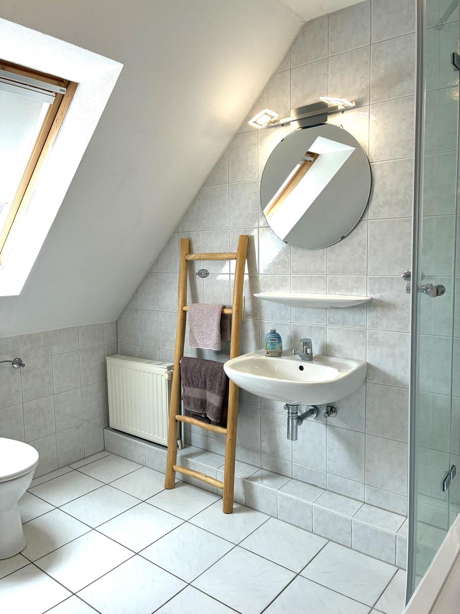 Badezimmer mit Dusche, Waschbecken und Holzhandtuchständer unter Dachschrägen.