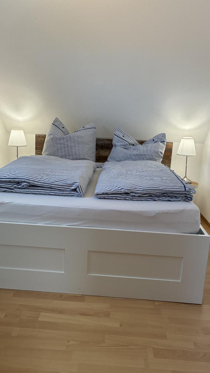 Doppelbett mit blau-weiß gestreifter Bettwäsche und zwei Nachttischen mit Lampen.