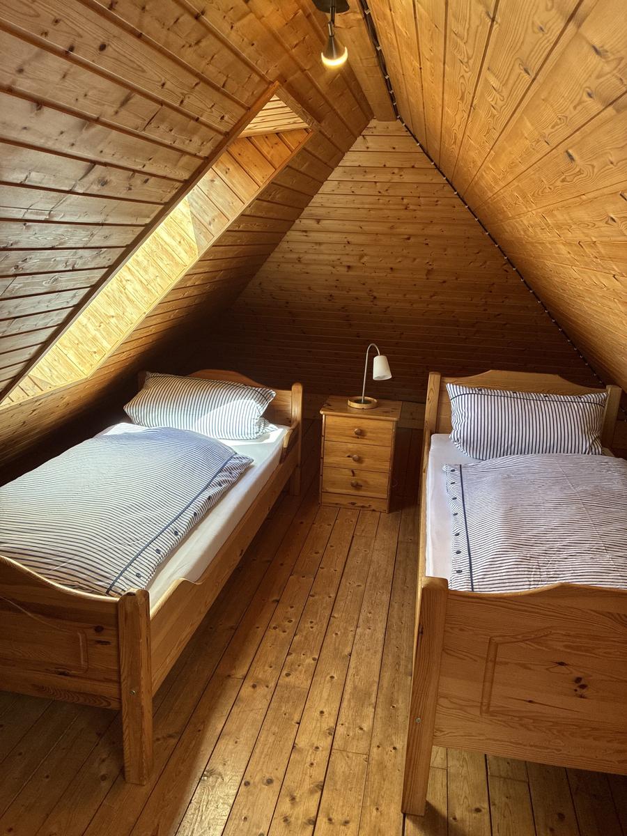 Zwei Einzelbetten mit Streifenbetten in einem Dachzimmer mit Holzwand und Holzboden.