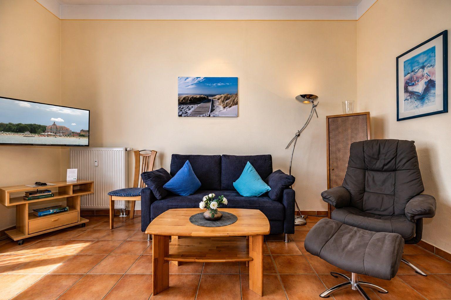 Wohnzimmer mit Sofa, Sessel, Fernseher und Holztisch.