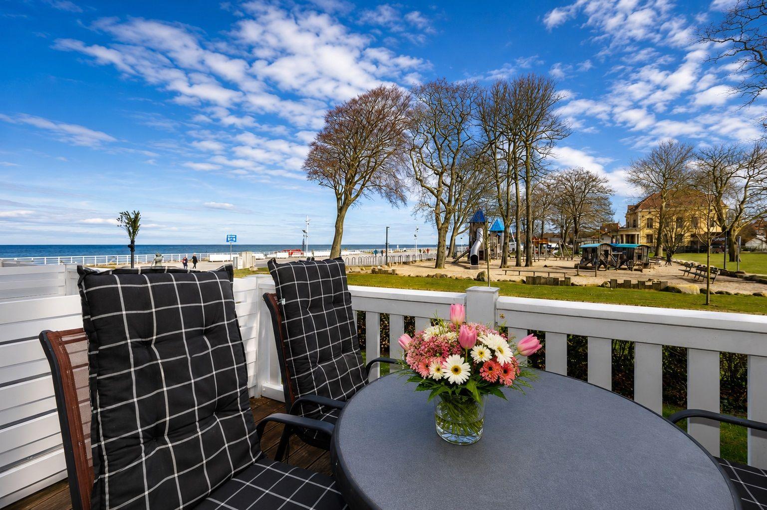 Terrasse mit Tisch und Stühlen, Blick auf Strand und Spielplatz.