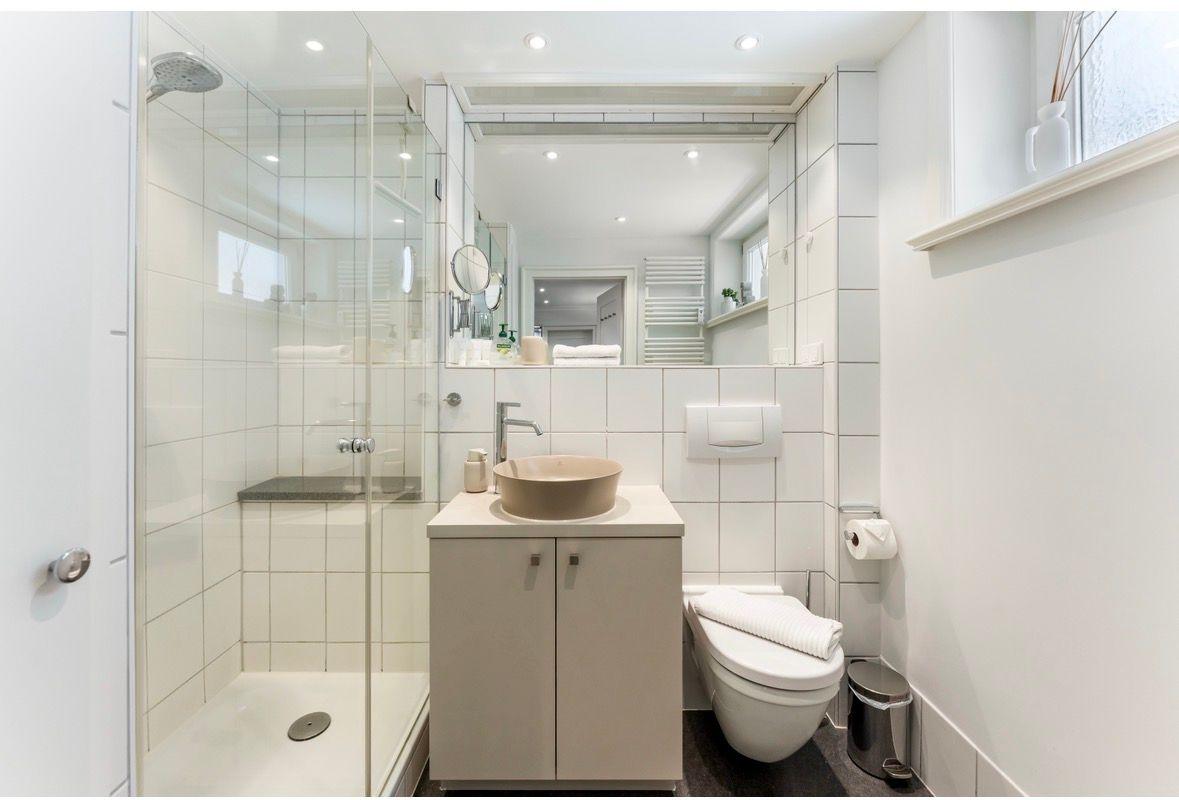 Badezimmer mit Dusche, Waschbecken und Toilette. Weiße Fliesen und Spiegel.