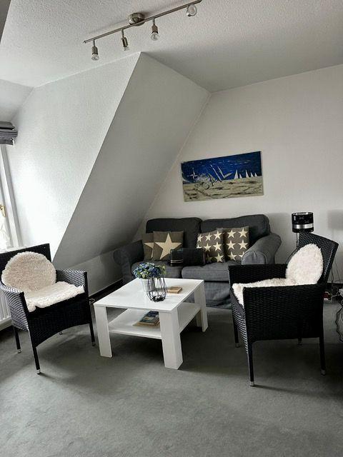 Wohnzimmer mit Sofa, zwei Sesseln und Couchtisch unter schrägen Dachdecken.