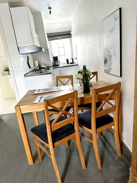 Essbereich mit Holztisch und Stühlen, Küche im Hintergrund, Wandbild an der Wand.