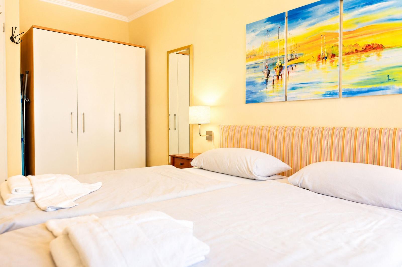 Schlafzimmer mit Doppelbett, Kleiderschrank und Wandbild mit Schiffen.