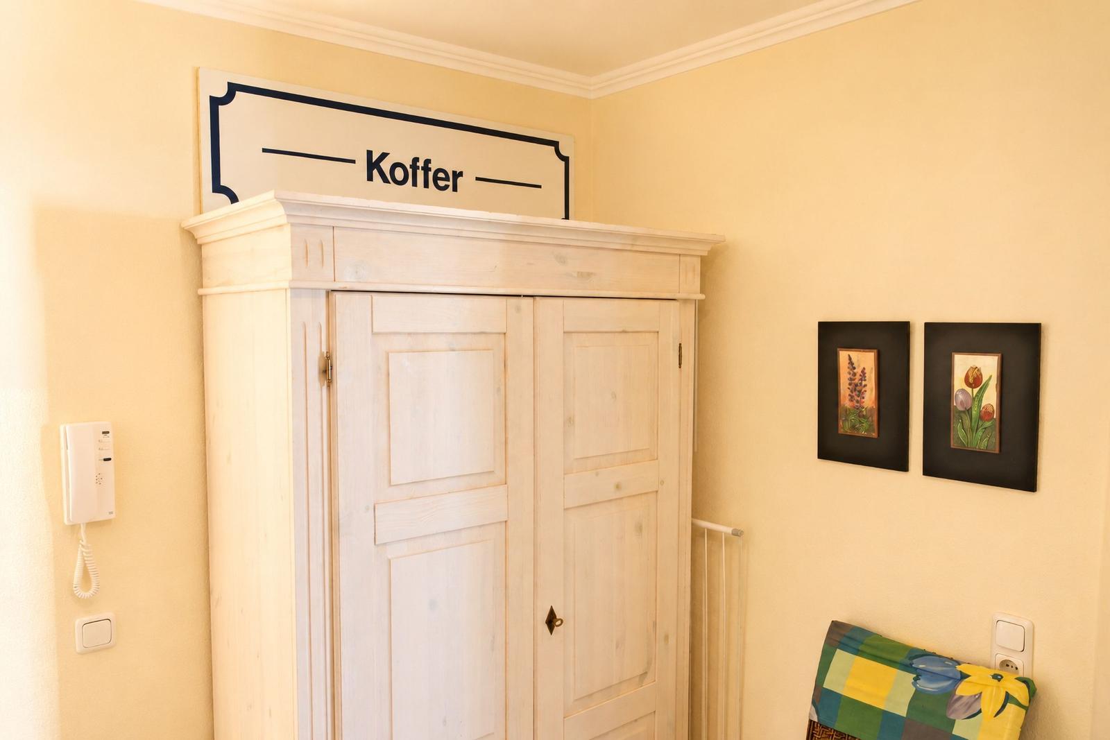Haus mit Kleiderschrank, Wandbildern und Schild Koffer.