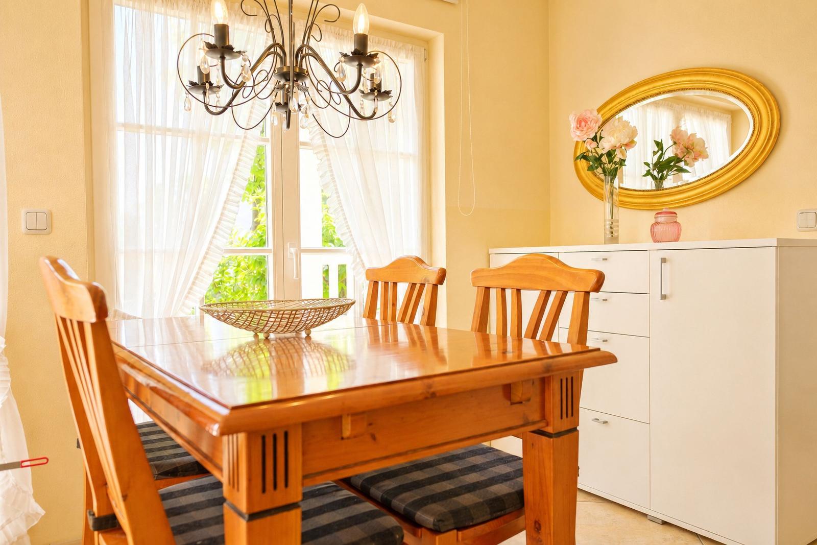 Esszimmer mit Holztisch, Stühlen und Fenster. Hängelampe, Spiegel und Schrank sind sichtbar.