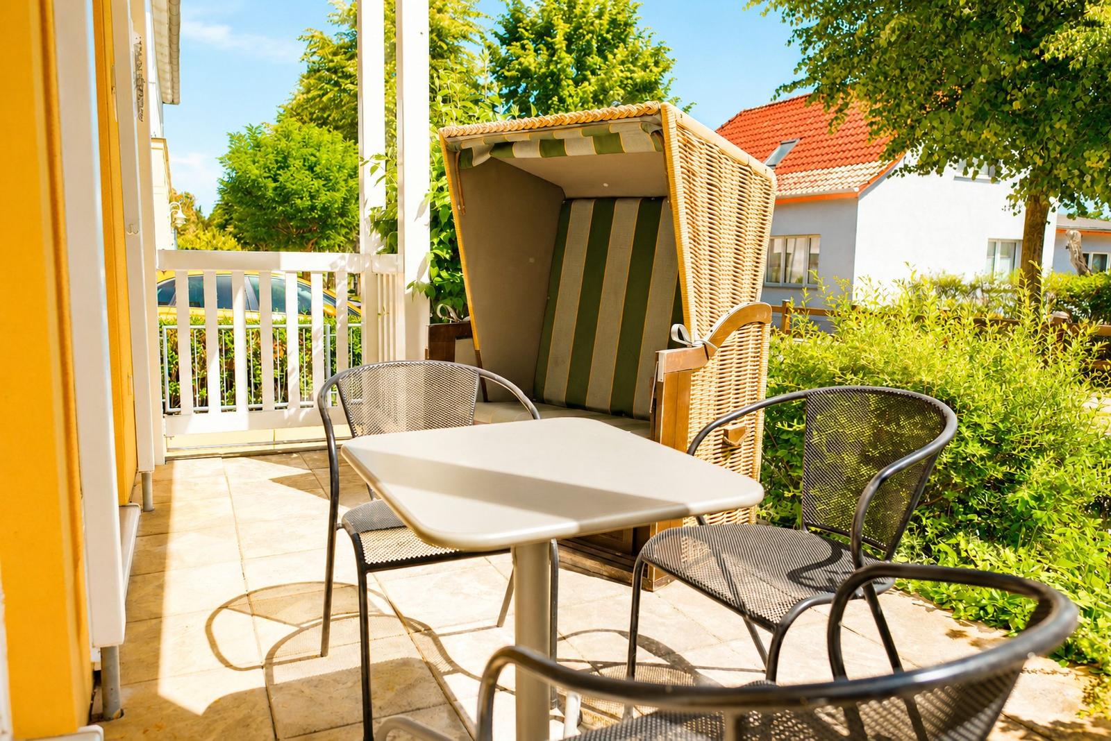 Terrasse mit Tisch, Stühlen und Strandkorb. Grün umgebene Außenterrasse mit Blick auf Haus.