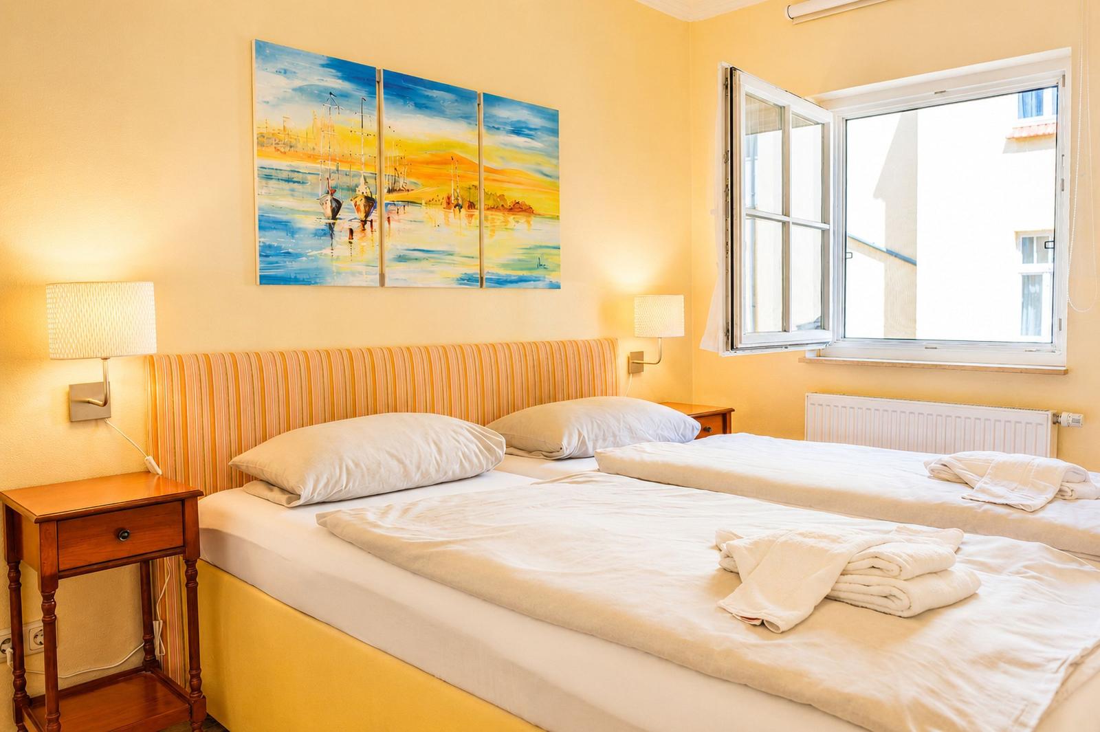 Zwei Betten mit weißen Laken, Wandbild und Fenster mit Blick nach draußen.