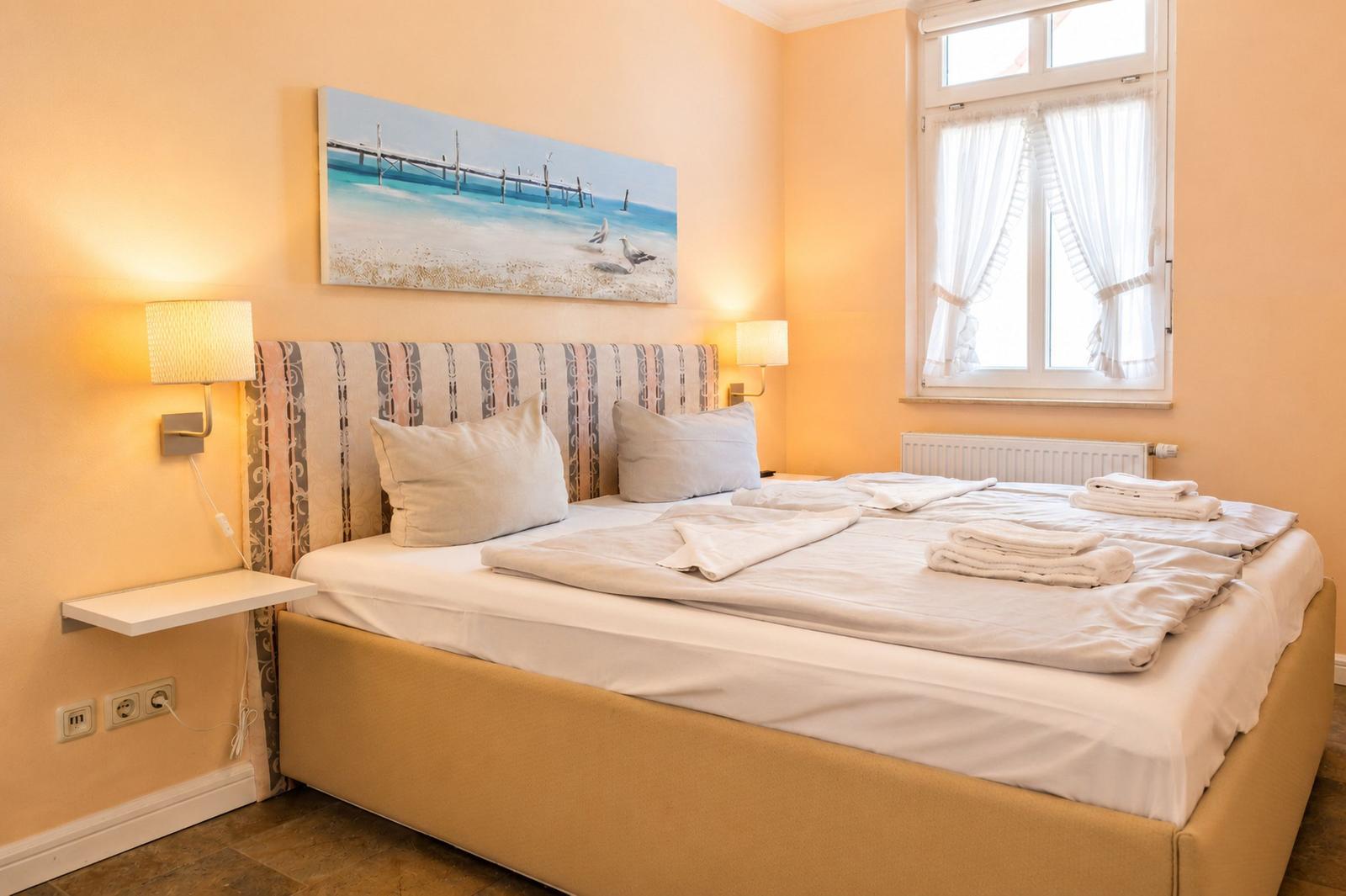 Schlafzimmer mit Bett, Wandbild und Fenster mit Vorhängen.