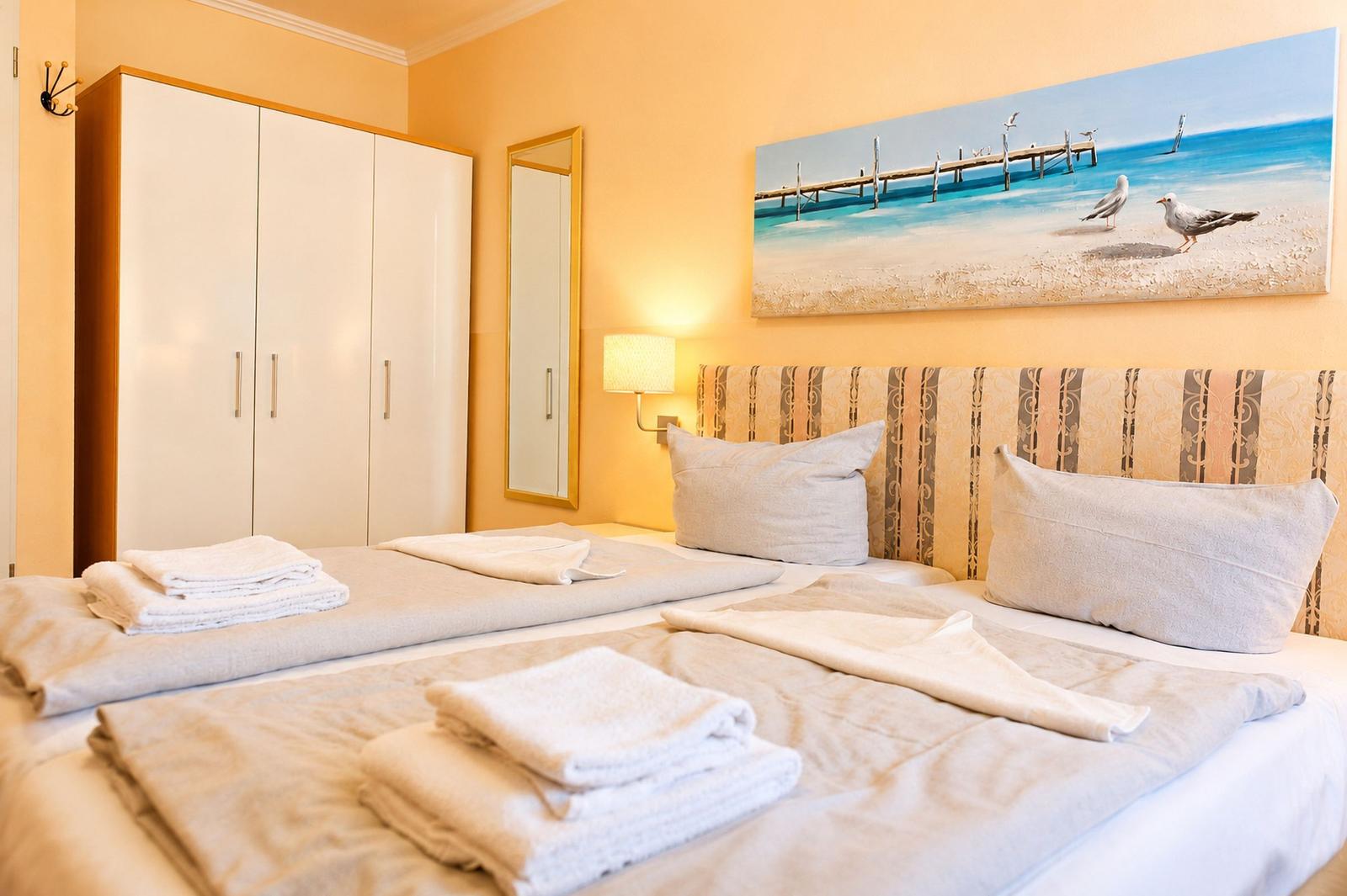 Schlafzimmer mit Doppelbett, Kleiderschrank und Strandbild an der Wand.