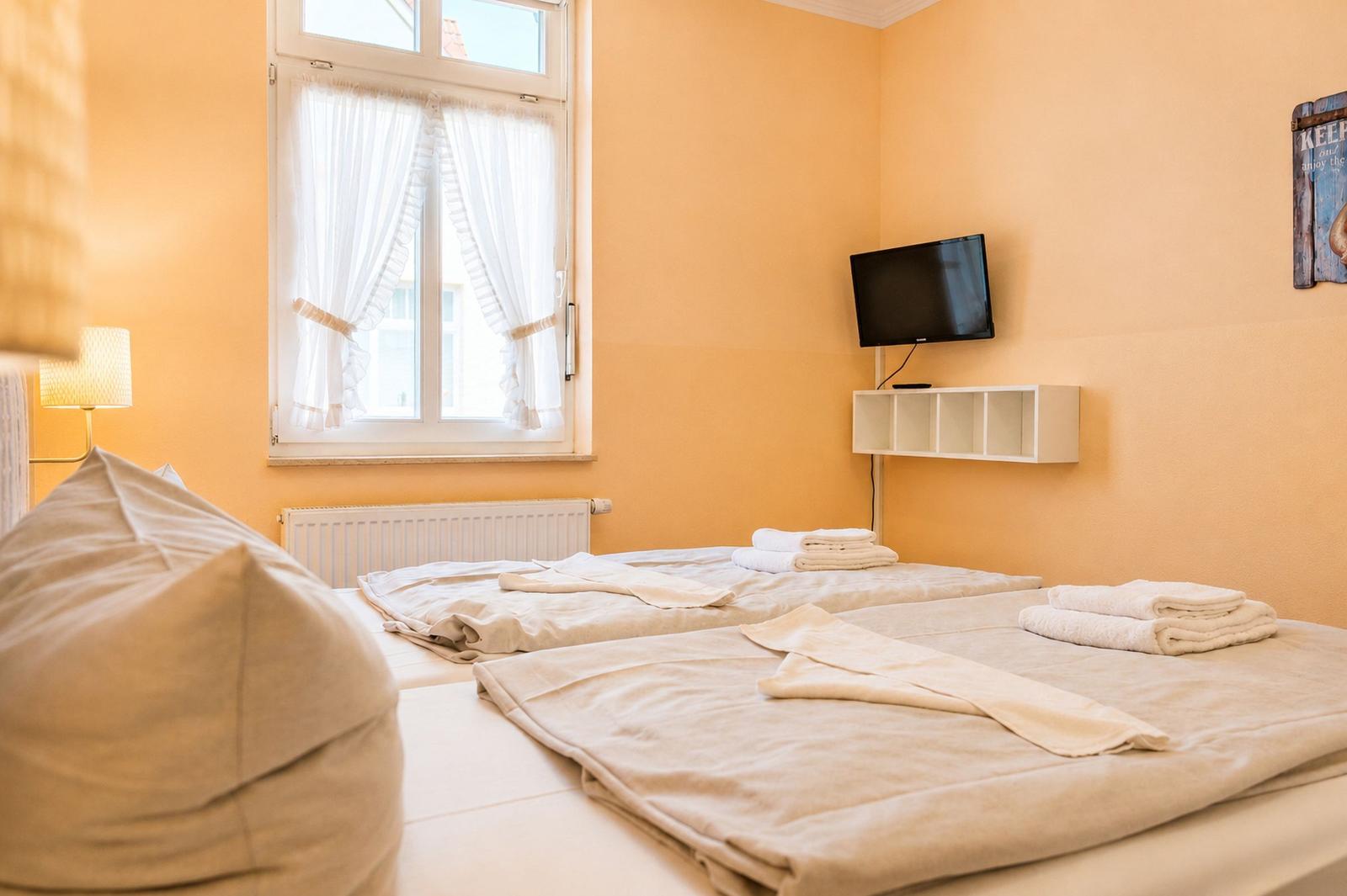 Zwei Betten mit Bettwäsche, Fernseher und Fenster mit weißen Vorhängen.
