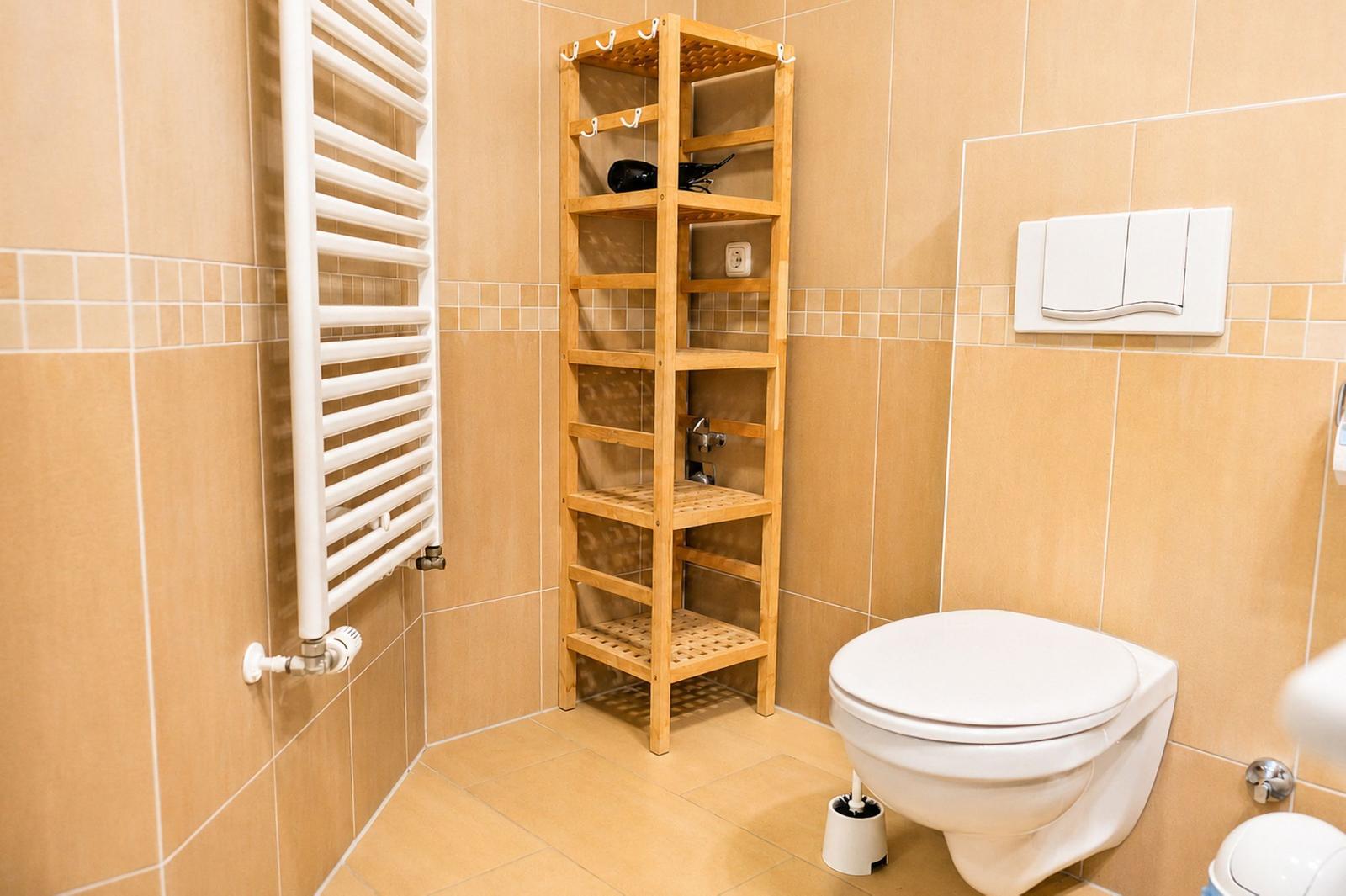 Badezimmer mit Toilette, Holzregal und Heizkörper an der Wand.