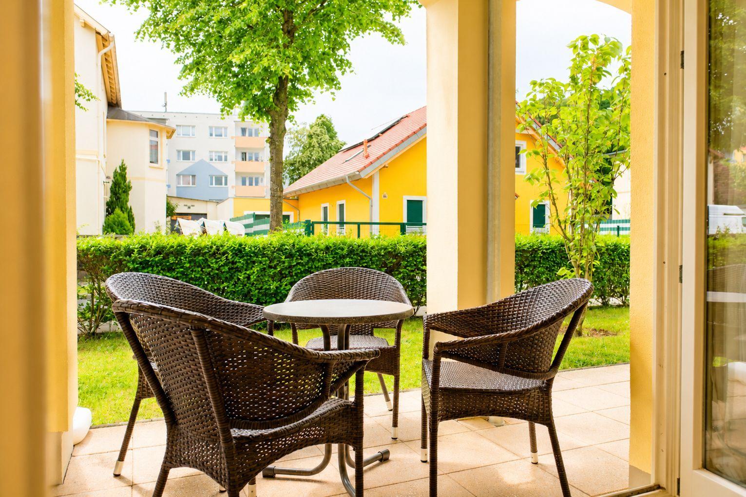 Terrasse mit Tisch und drei Stühlen. Blick auf grünen Rasen und Häuser im Hintergrund.