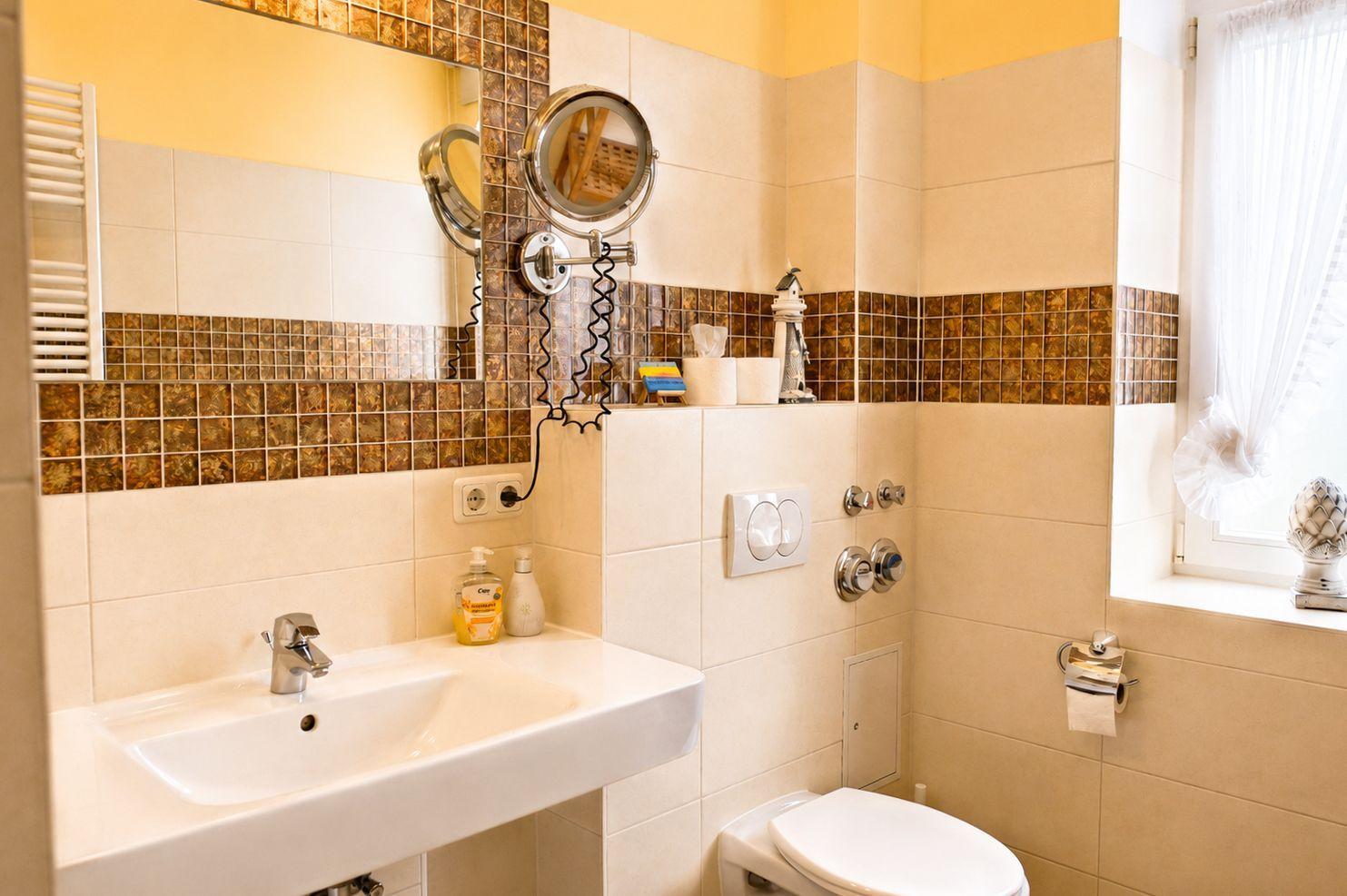 Badezimmer mit Waschbecken, Toilette und Spiegel. Wandverkleidung mit Mosaikfliesen.