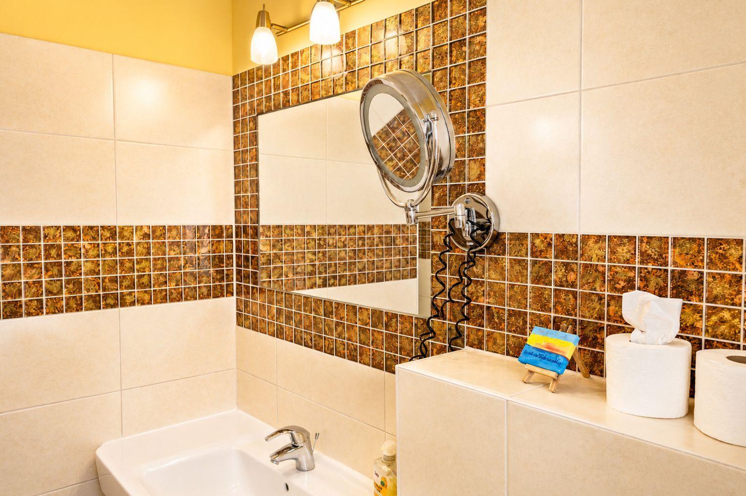 Badezimmer mit Waschbecken, Spiegel und Mosaikfliesen an den Wänden.