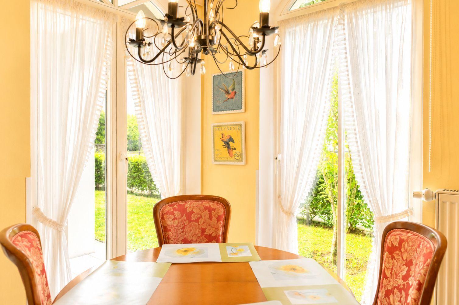Esszimmer mit Tisch, Stühlen und Fenstern zum Garten.