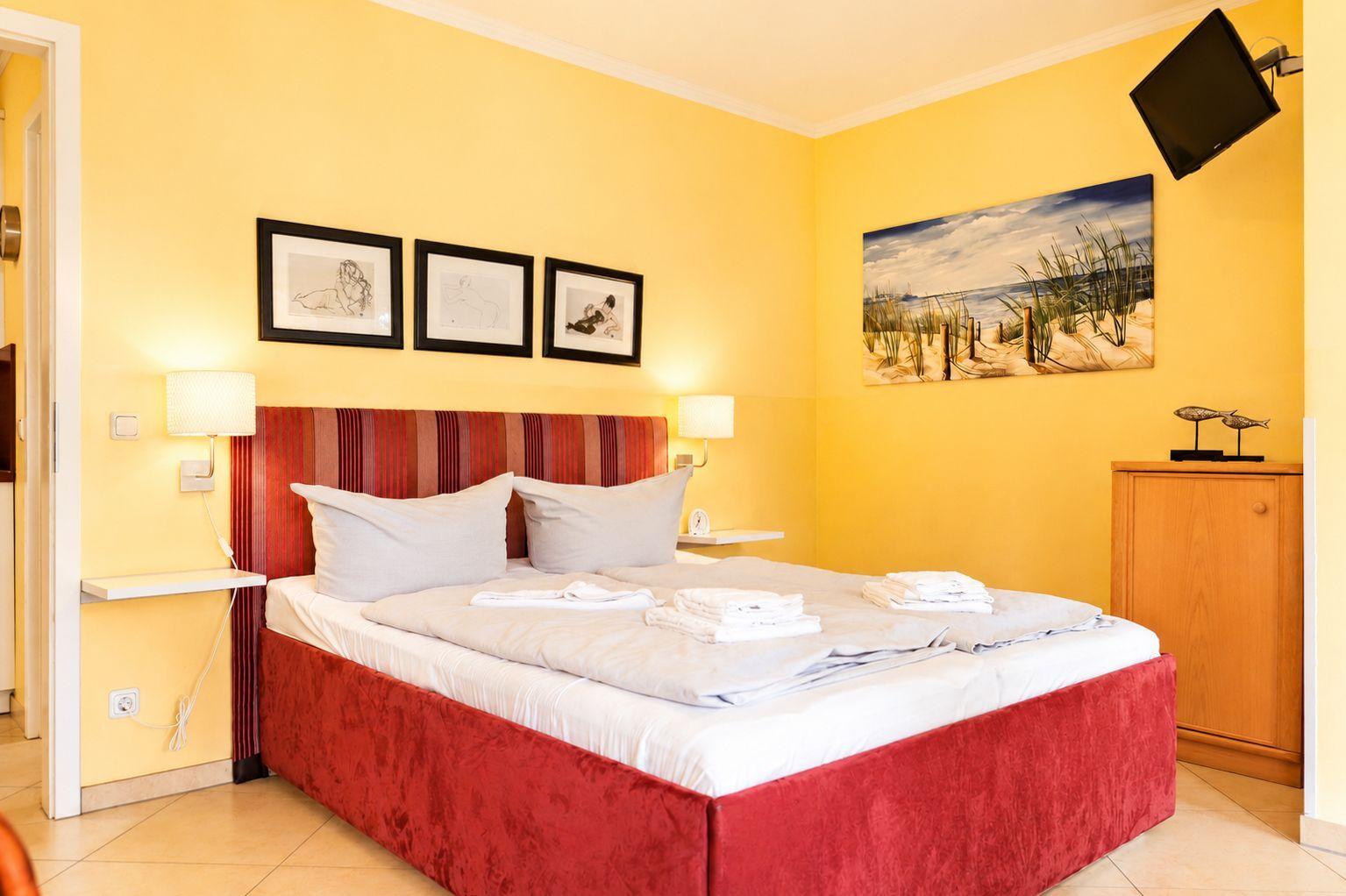 Schlafzimmer mit Bett, Wandbild und Schrank. Wände sind gelb gestrichen.